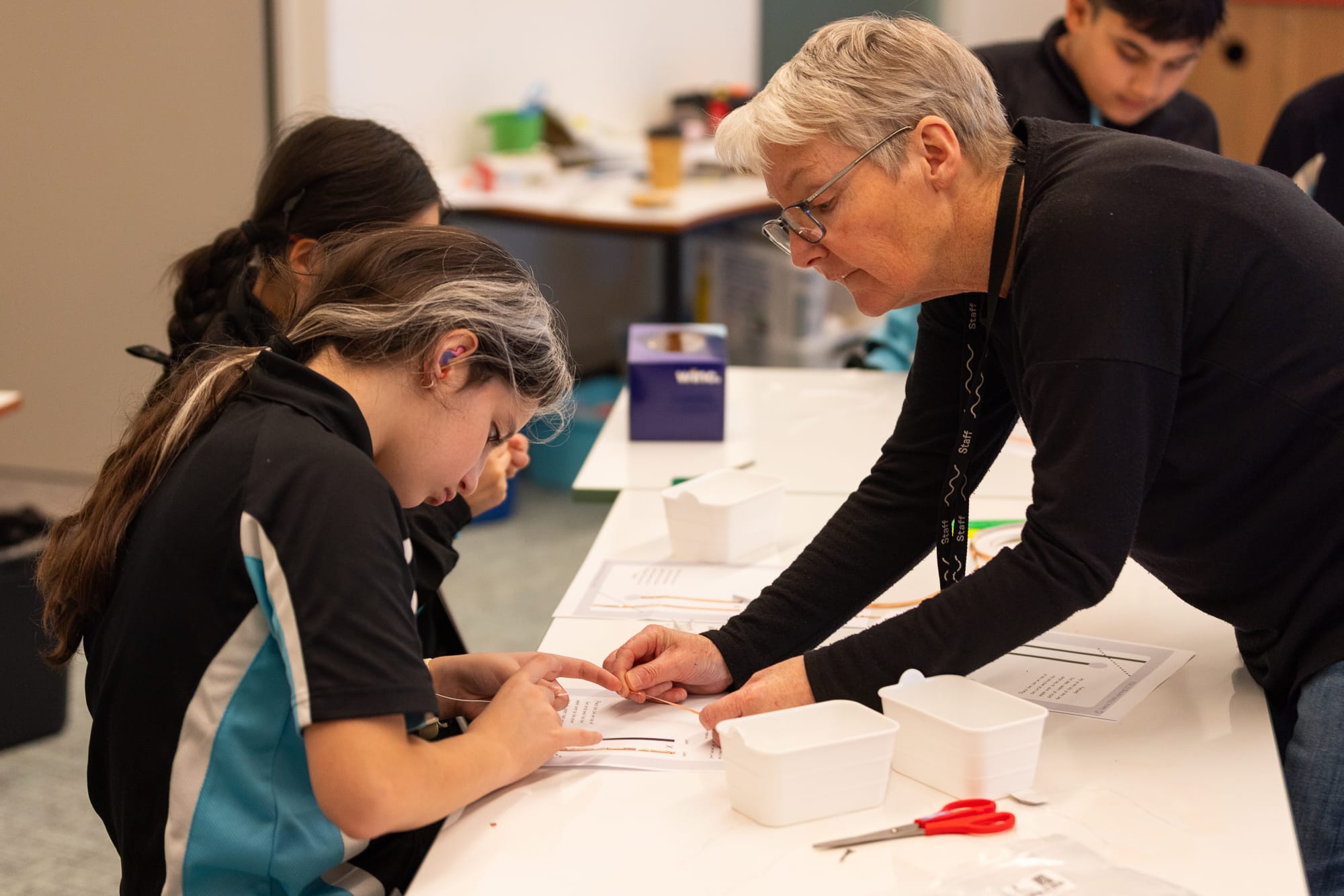A young student in NextSense uniform sitting at a desk working with support from a teacher.